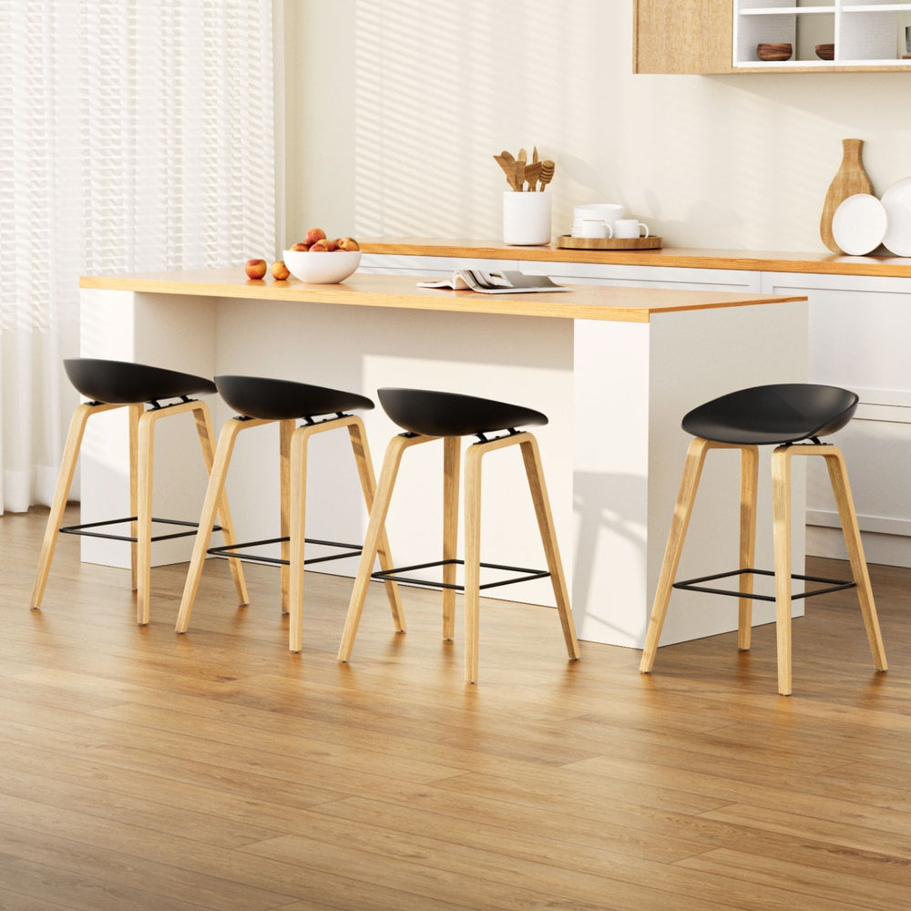 Four black bar stools with wooden legs in a kitchen setting.