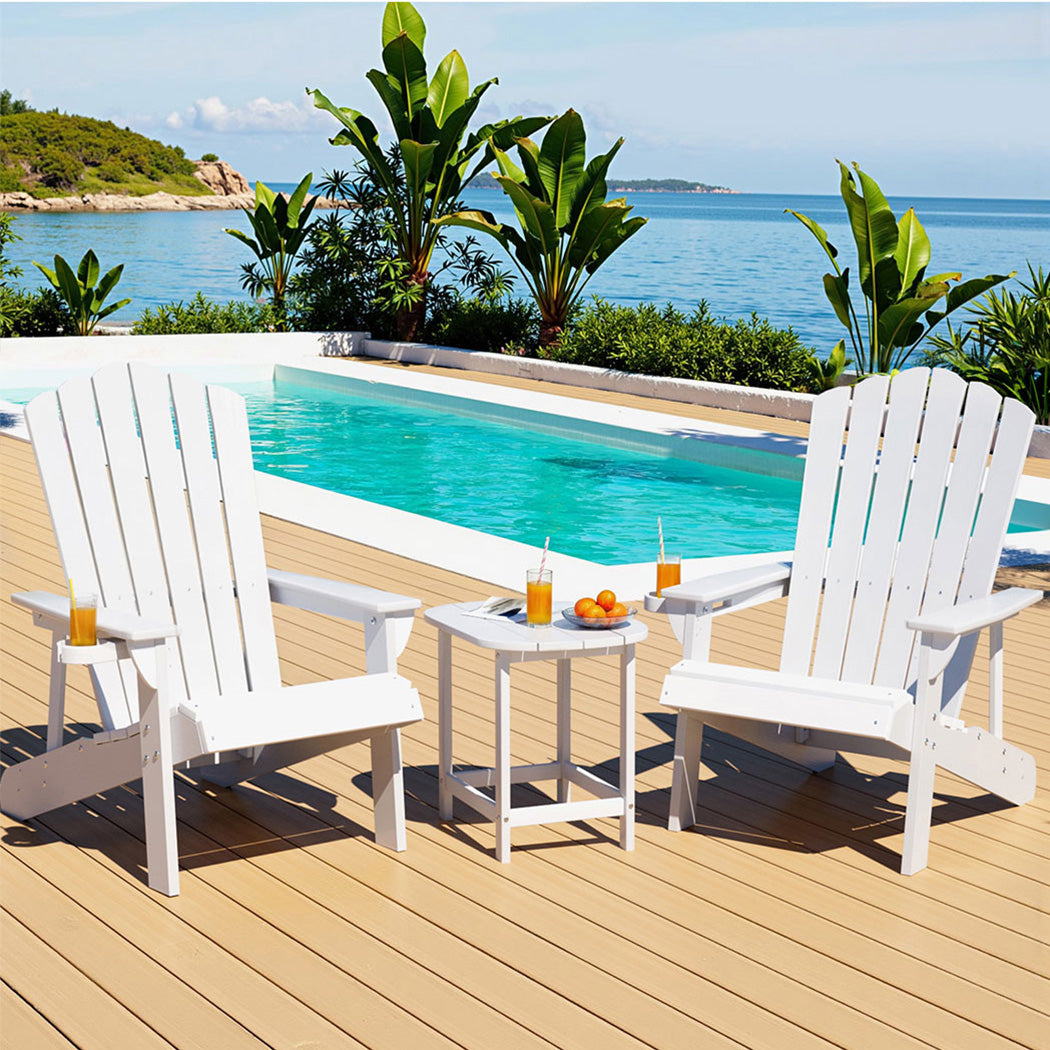 Two white chairs and a small table by a pool with a scenic view of water and greenery.