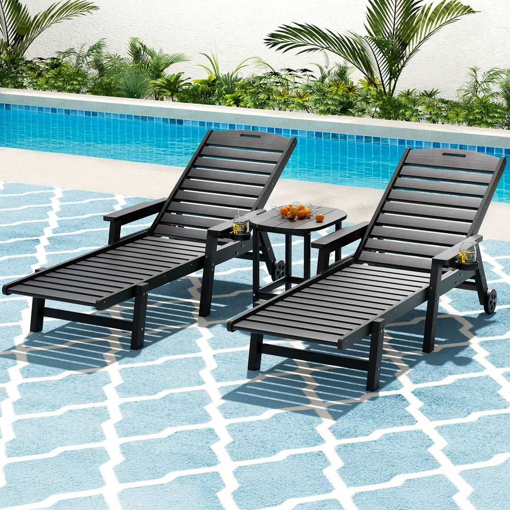 Two black lounge chairs and a small table by a pool with a garden in the background.