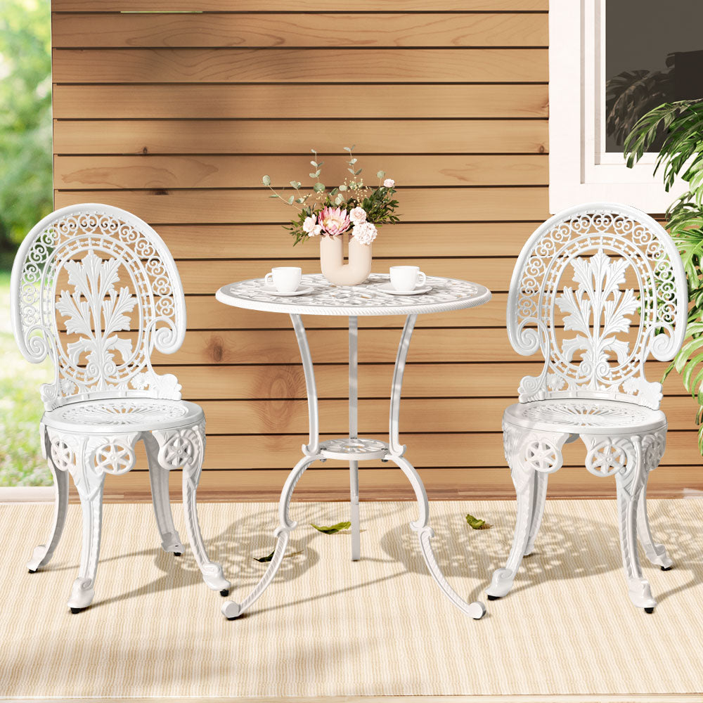 White metal outdoor furniture set with table and chairs against a wooden wall.