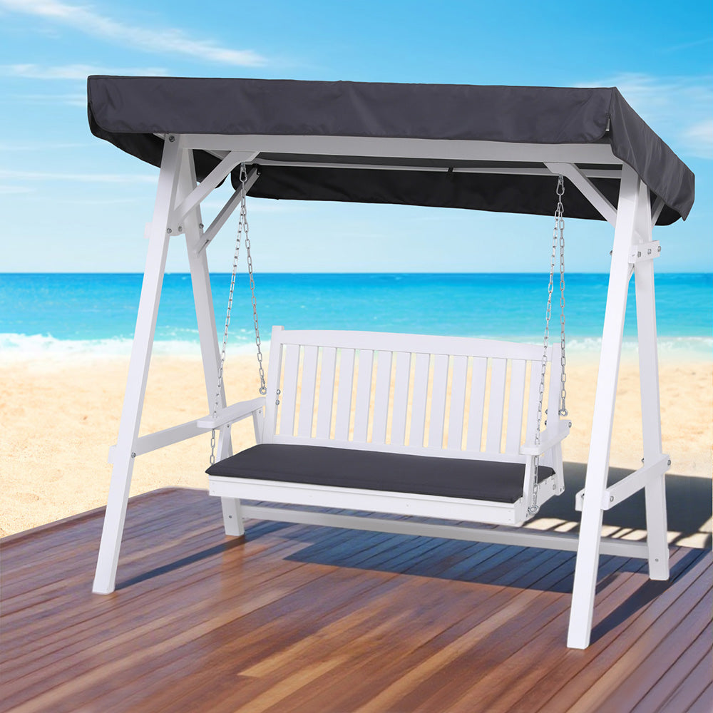 White outdoor swing with black canopy on a wooden deck by the beach