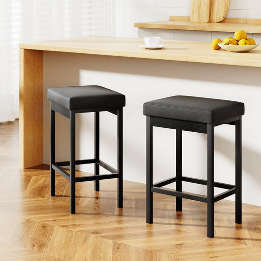 Two black bar stools in front of a wooden counter with a white wall background.