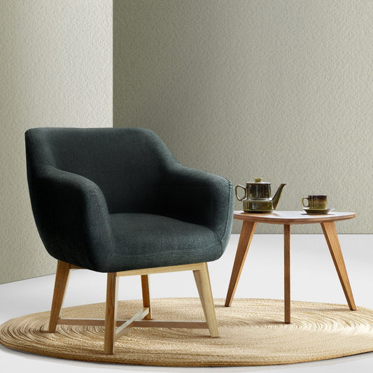 Dark gray armchair with wooden legs in a minimalistic room with a small table and teapot.