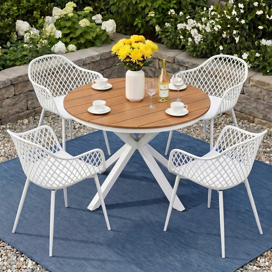 Outdoor dining set with a wooden table and white chairs on a blue rug, surrounded by flowers and plants.
