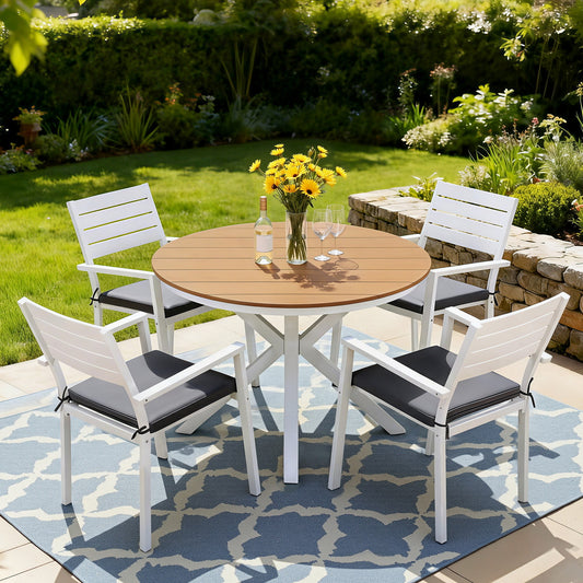 Outdoor patio set with round wooden table and four white chairs on a patterned rug.