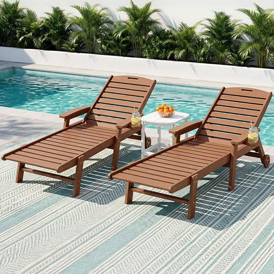 Two wooden lounge chairs by a pool with a small table and fruit on a striped deck.
