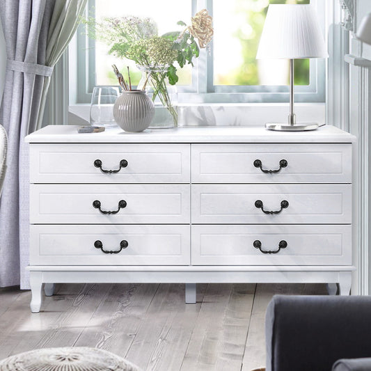 White dresser with black handles in a room with a window and decorative items.