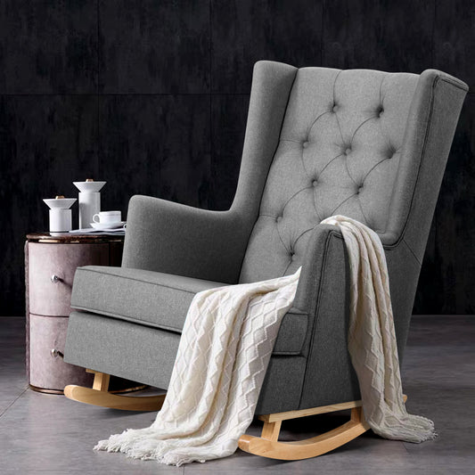 Gray upholstered rocking chair with a white blanket on a dark background